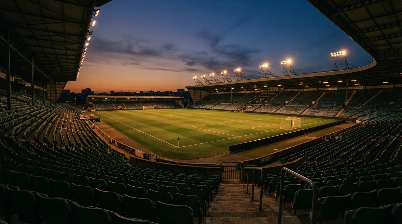 An empty football stadium with floodlight masts at dusk