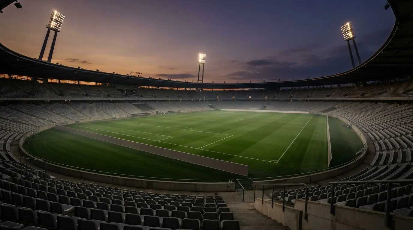 An empty football stadium with floodlight masts at dusk